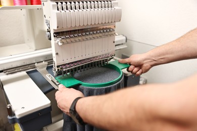 Photo of Man using embroidery machine to make design on T-shirt indoors, closeup