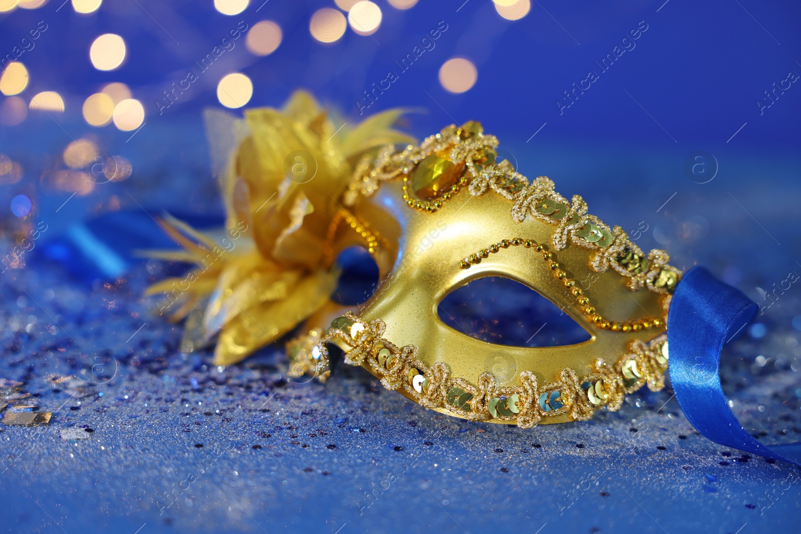 Photo of Beautiful carnival mask on blue glitter background against blurred lights, closeup. Bokeh effect