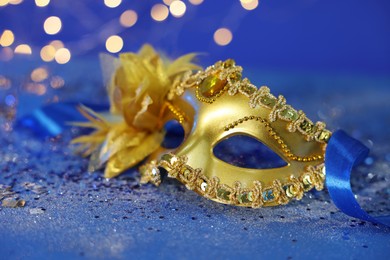 Photo of Beautiful carnival mask on blue glitter background against blurred lights, closeup. Bokeh effect