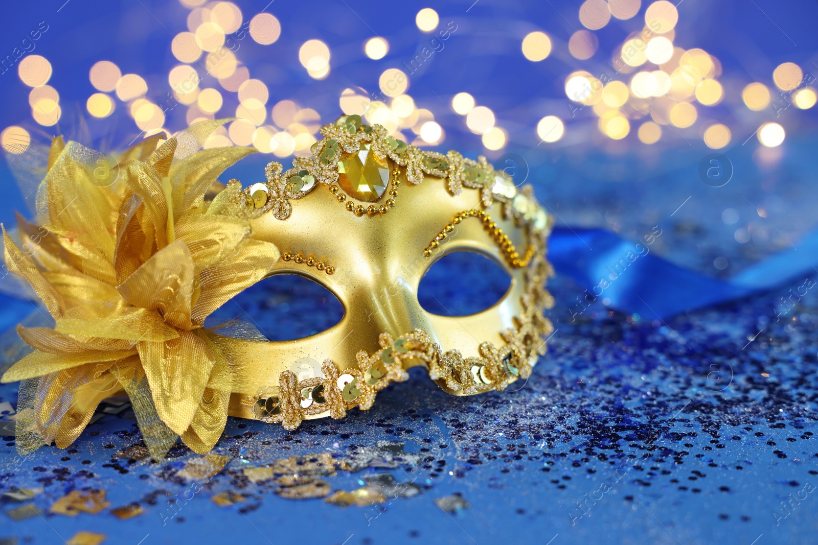 Photo of Beautiful carnival mask on blue glitter background against blurred lights, closeup. Bokeh effect