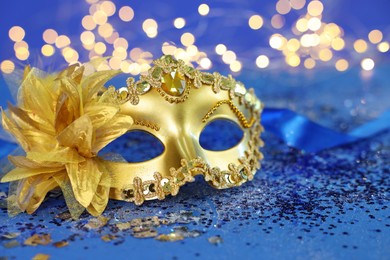 Photo of Beautiful carnival mask on blue glitter background against blurred lights, closeup. Bokeh effect