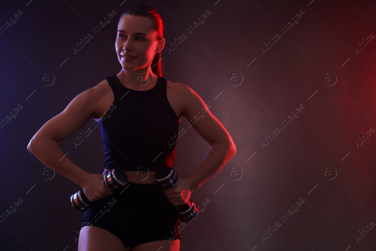 Photo of Woman exercising with dumbbells in smoke on dark background, space for text