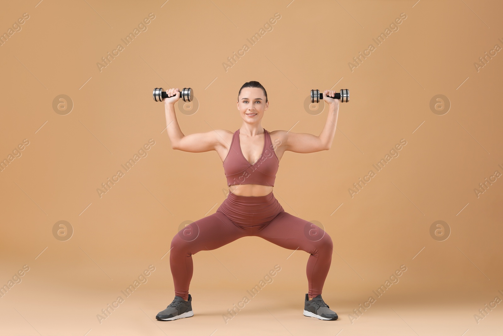 Photo of Woman exercising with dumbbells on beige background