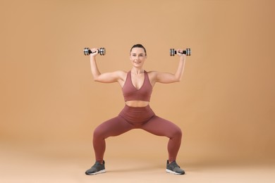 Photo of Woman exercising with dumbbells on beige background