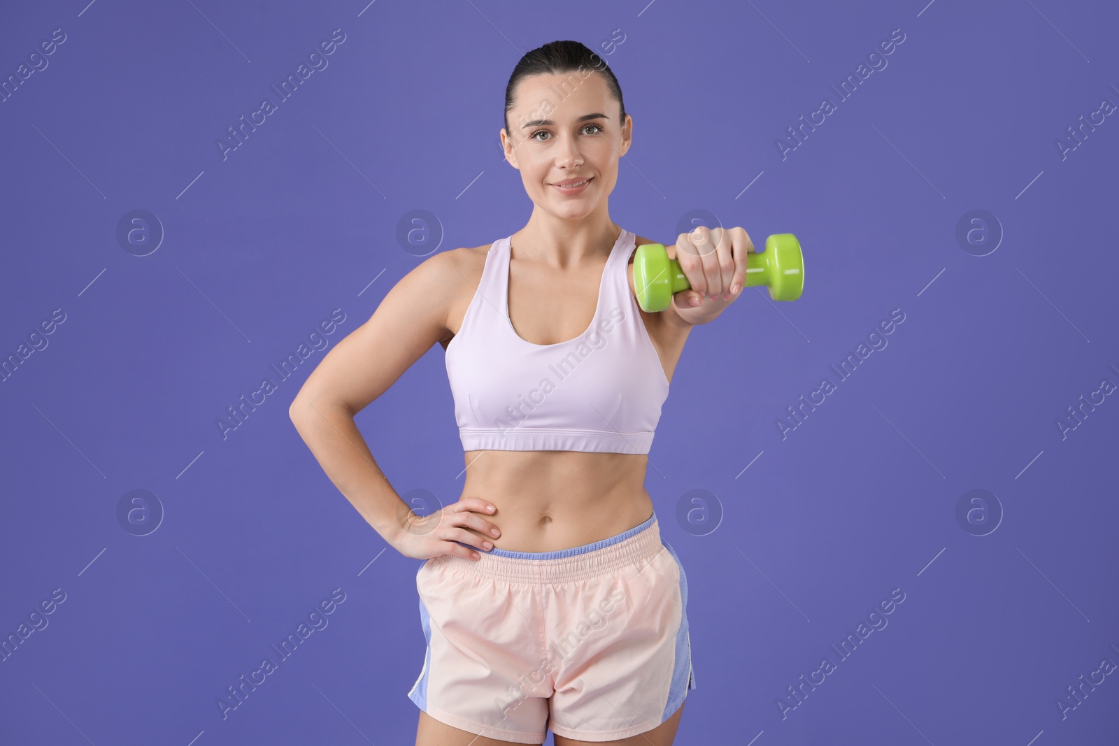 Photo of Woman exercising with dumbbell on purple background