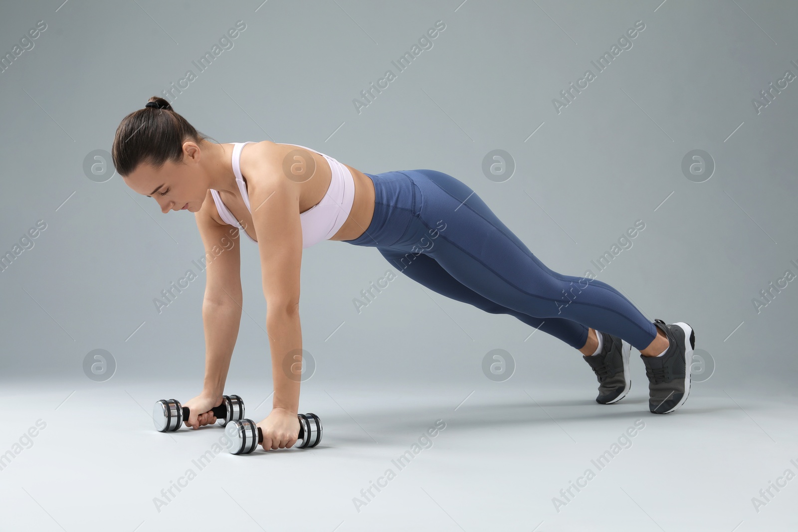 Photo of Woman exercising with dumbbells on light grey background