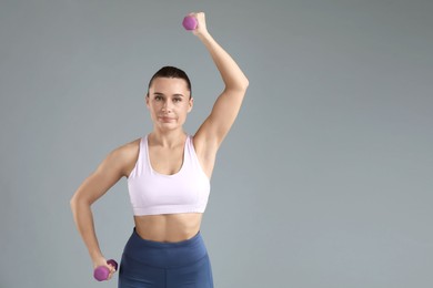 Photo of Woman exercising with dumbbells on light grey background, space for text