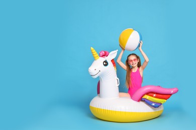 Photo of Happy little girl in beachwear with inflatable unicorn shaped ring and ball on light blue background, space for text