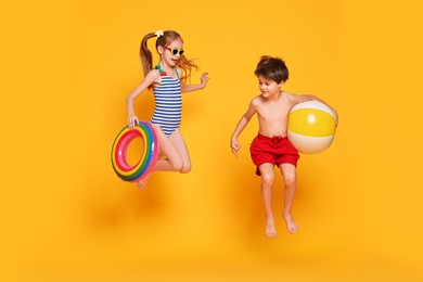 Photo of Little kids in beachwear jumping on orange background