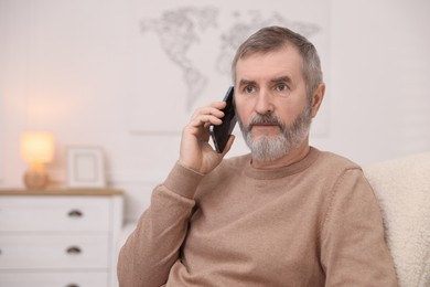 Photo of Mature man talking on smartphone at home. Space for text