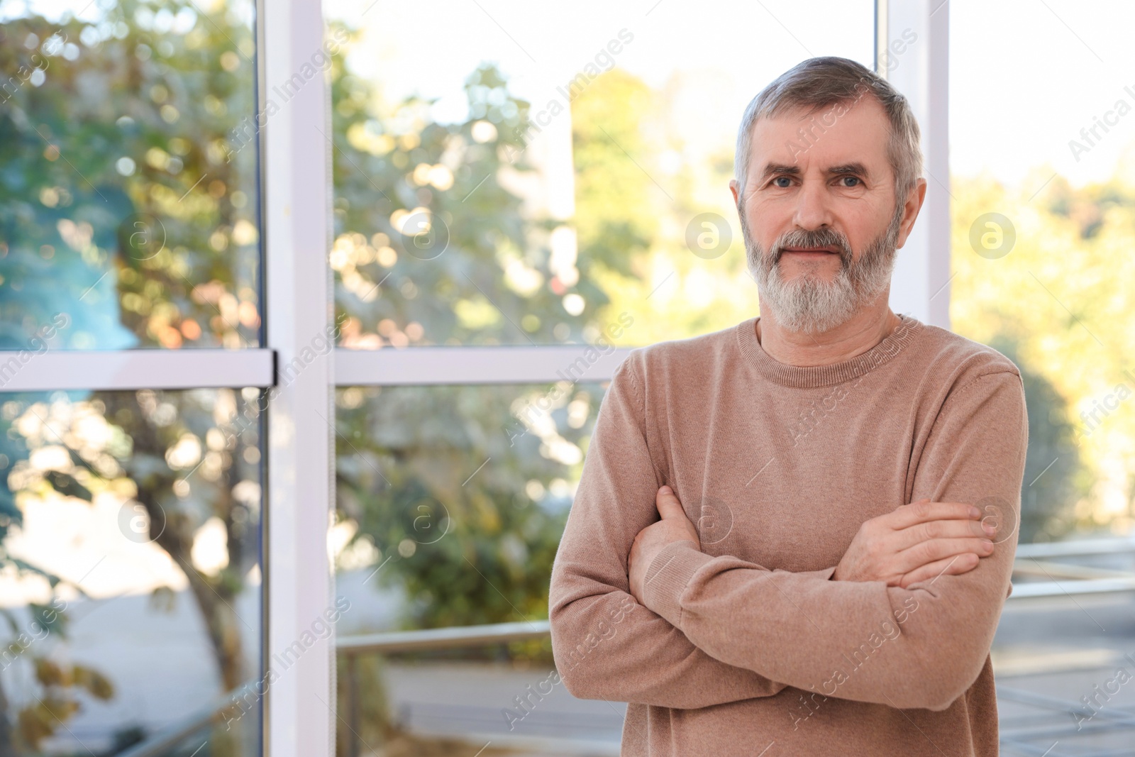 Photo of Mature man with crossed arms at home. Space for text