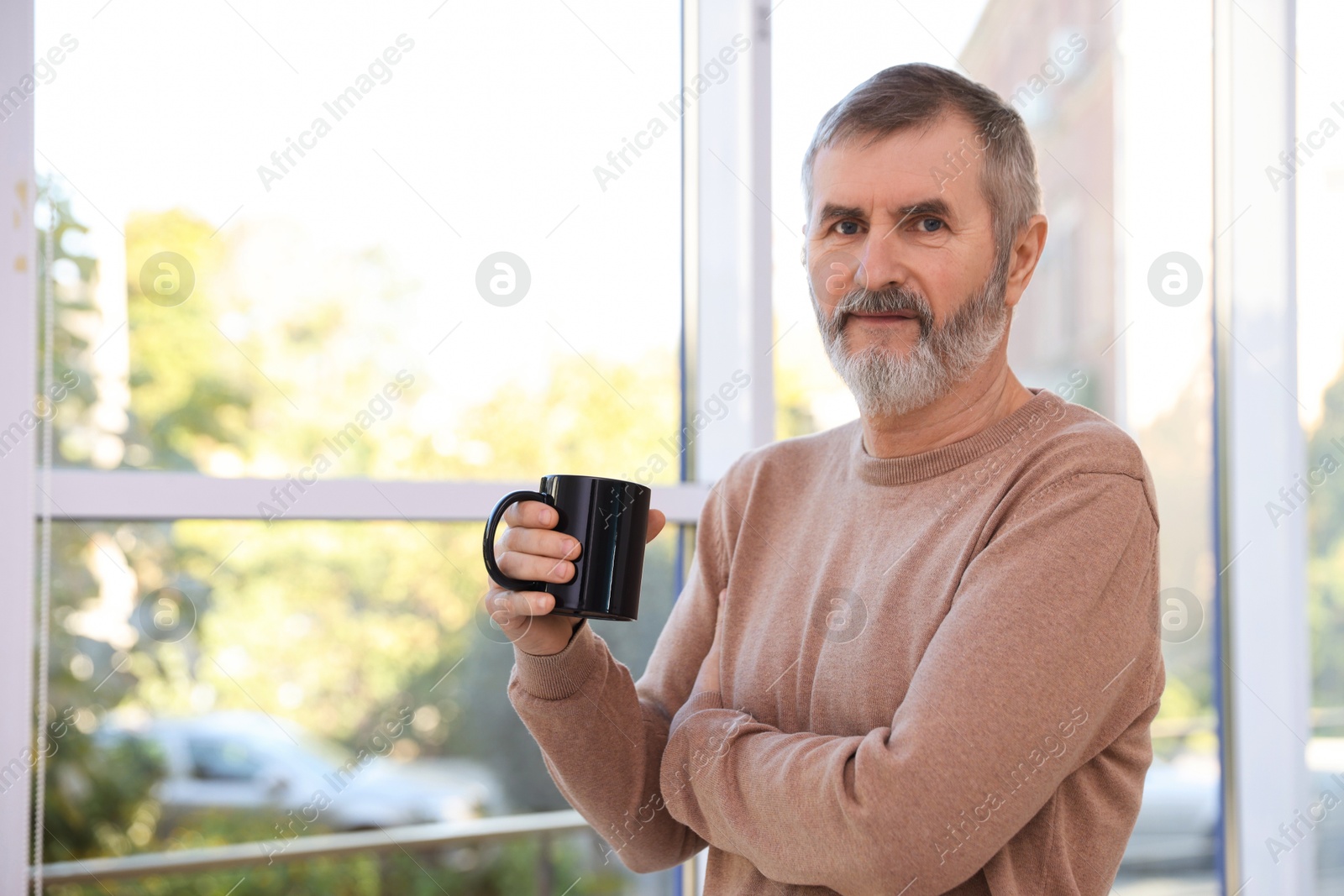 Photo of Mature man with cup of hot drink at home. Space for text