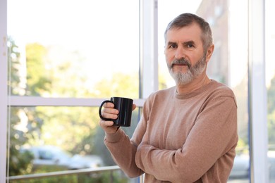 Photo of Mature man with cup of hot drink at home. Space for text