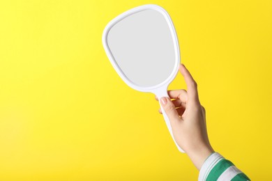 Woman holding small mirror on yellow background, closeup. Space for text