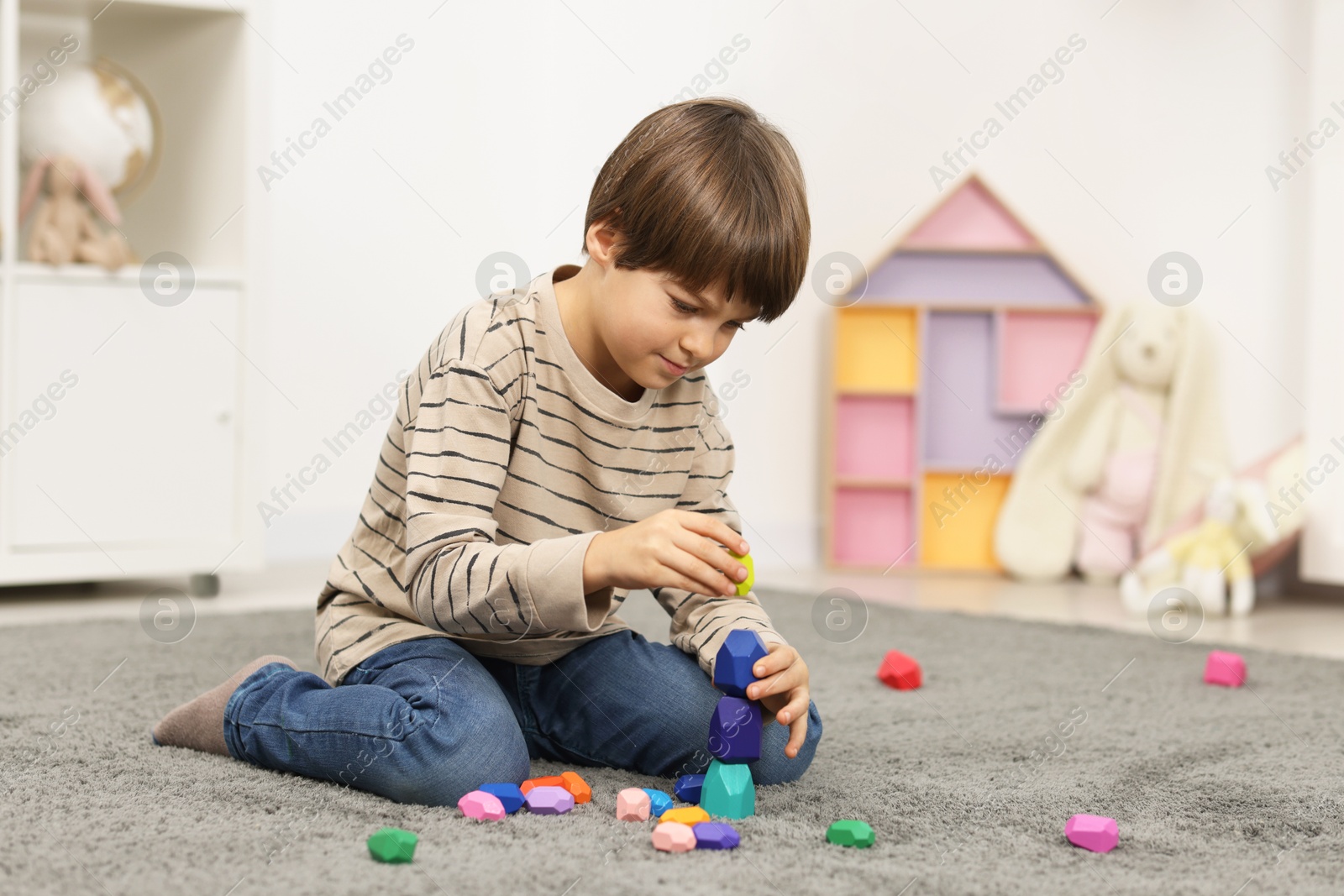 Photo of Boy playing with balancing stones on floor indoors