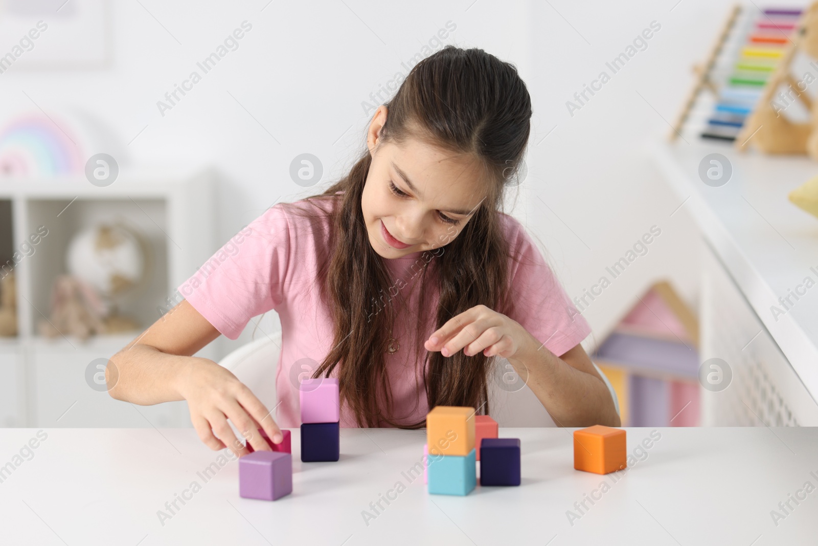 Photo of Happy girl with colorful cubes at table indoors