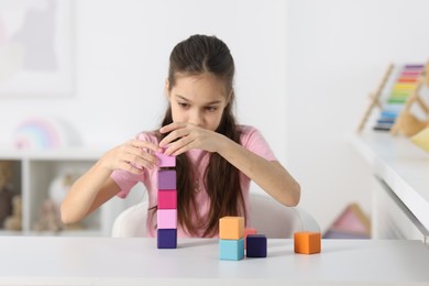 Photo of Girl building tower of colorful cubes at table indoors