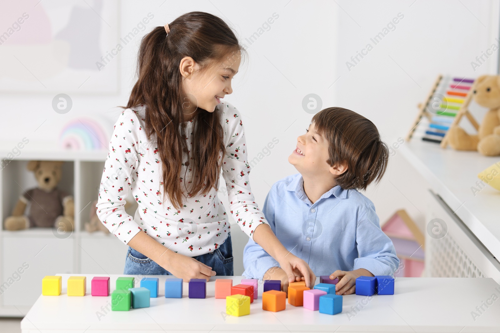 Photo of Children playing with colorful cubes at table indoors