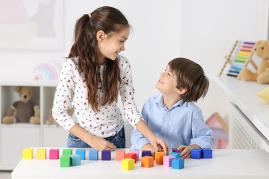 Children playing with colorful cubes at table indoors