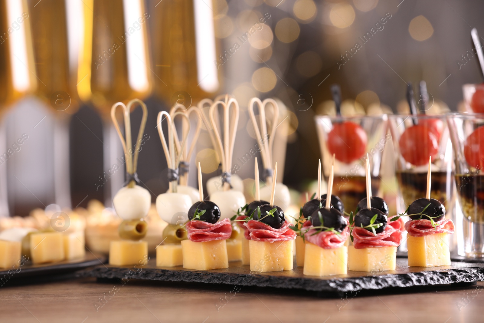 Photo of Many different tasty canapes on wooden table against blurred lights