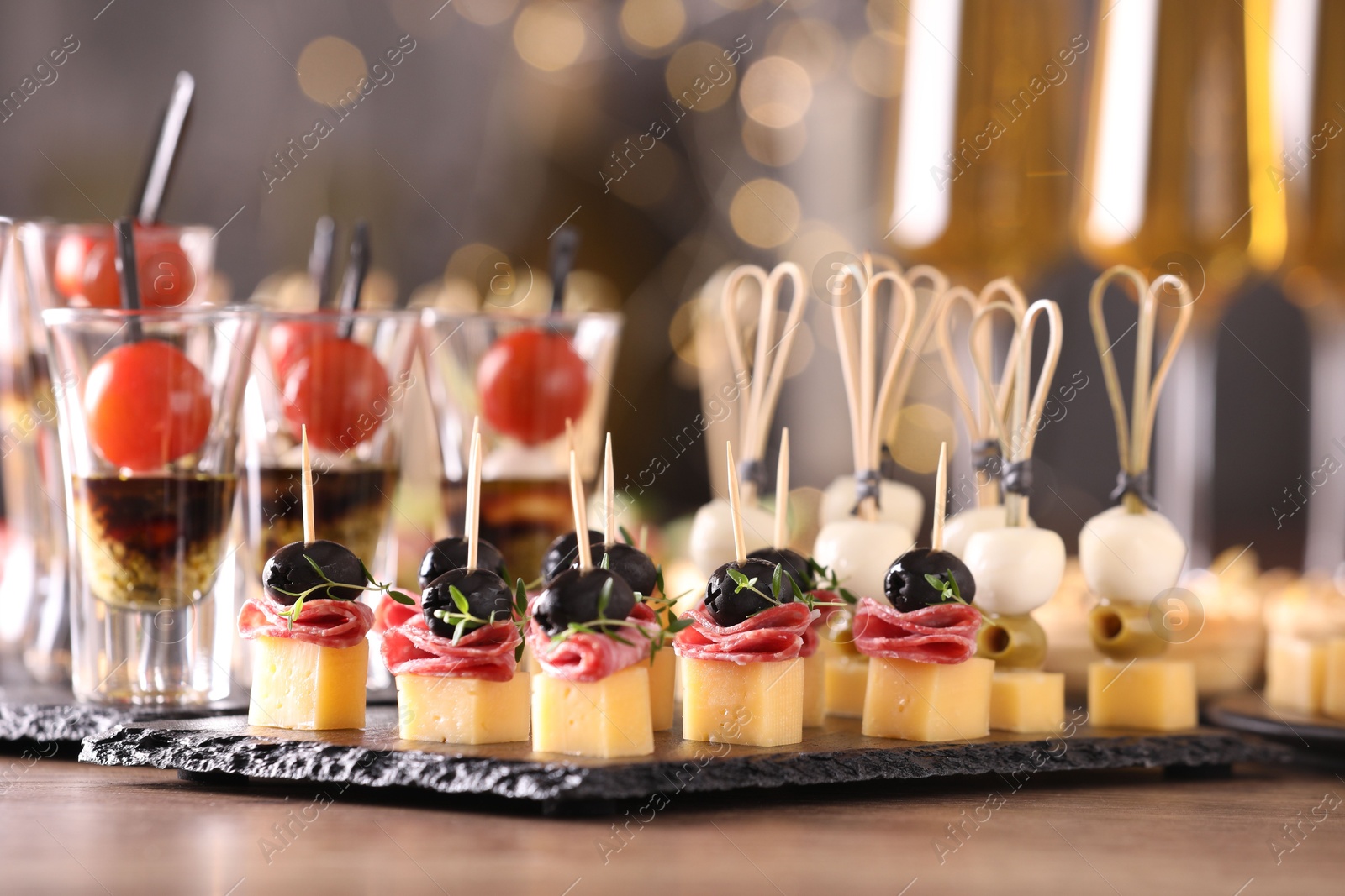 Photo of Many different tasty canapes on wooden table against blurred lights