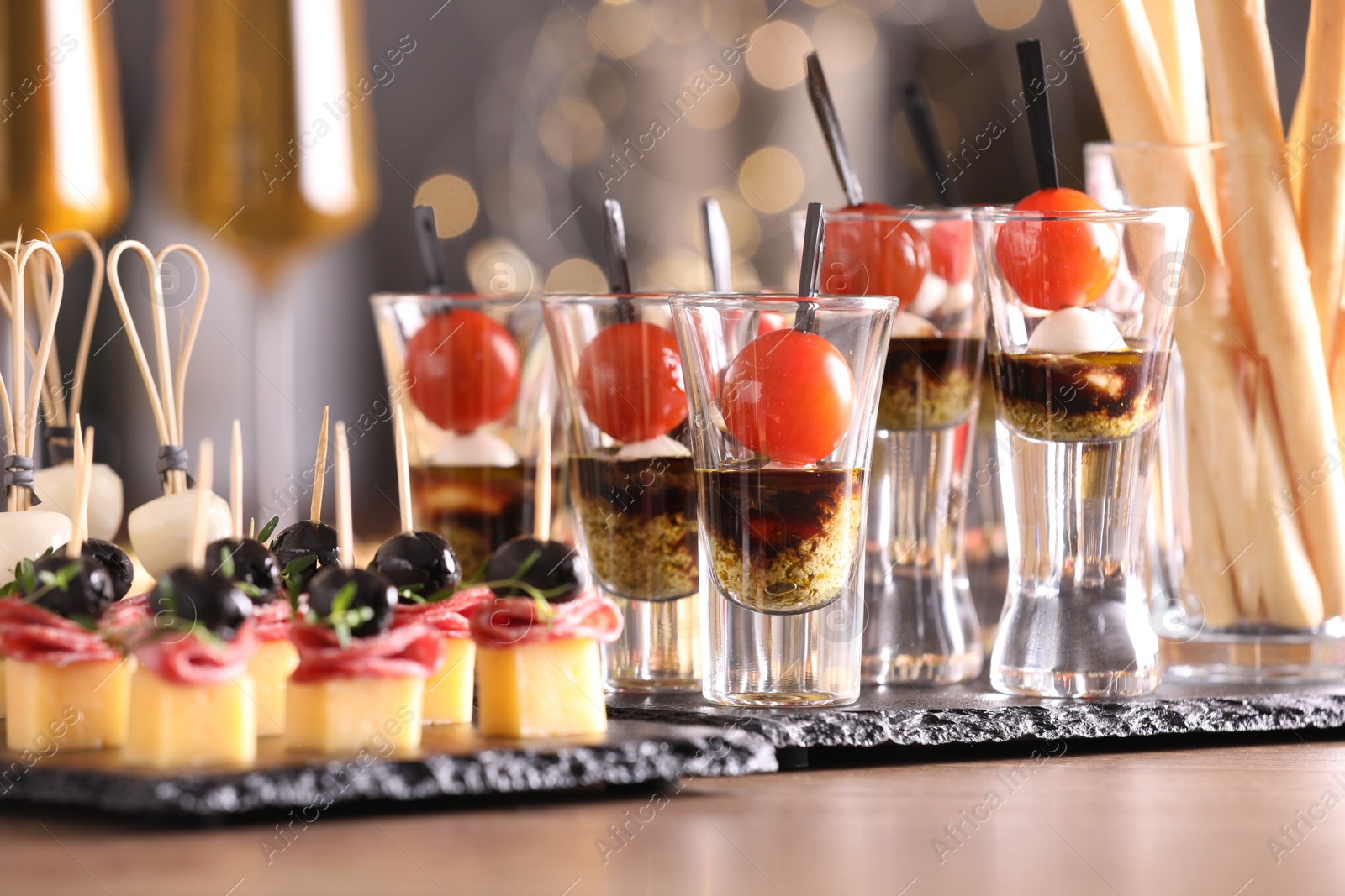 Photo of Many different tasty canapes on wooden table against blurred lights