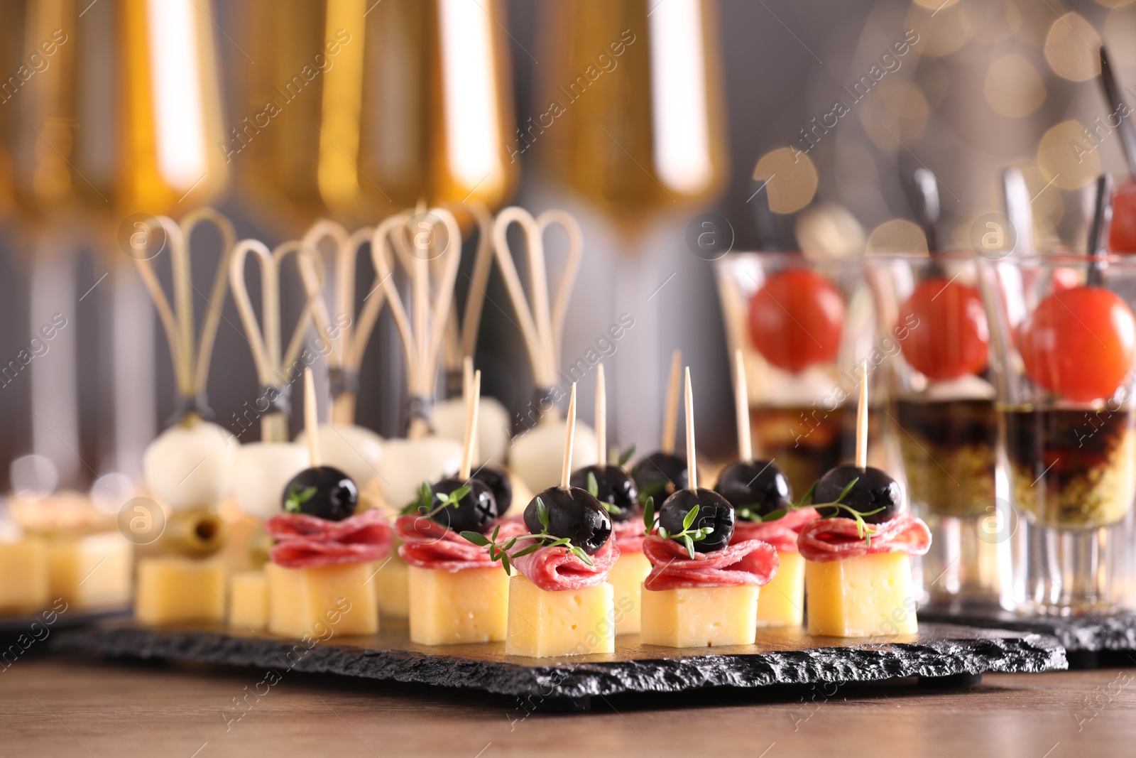 Photo of Many different tasty canapes and wine on wooden table against blurred lights