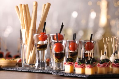 Photo of Many different tasty canapes on wooden table against blurred lights