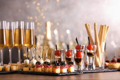 Photo of Many different tasty canapes and wine on wooden table against blurred lights