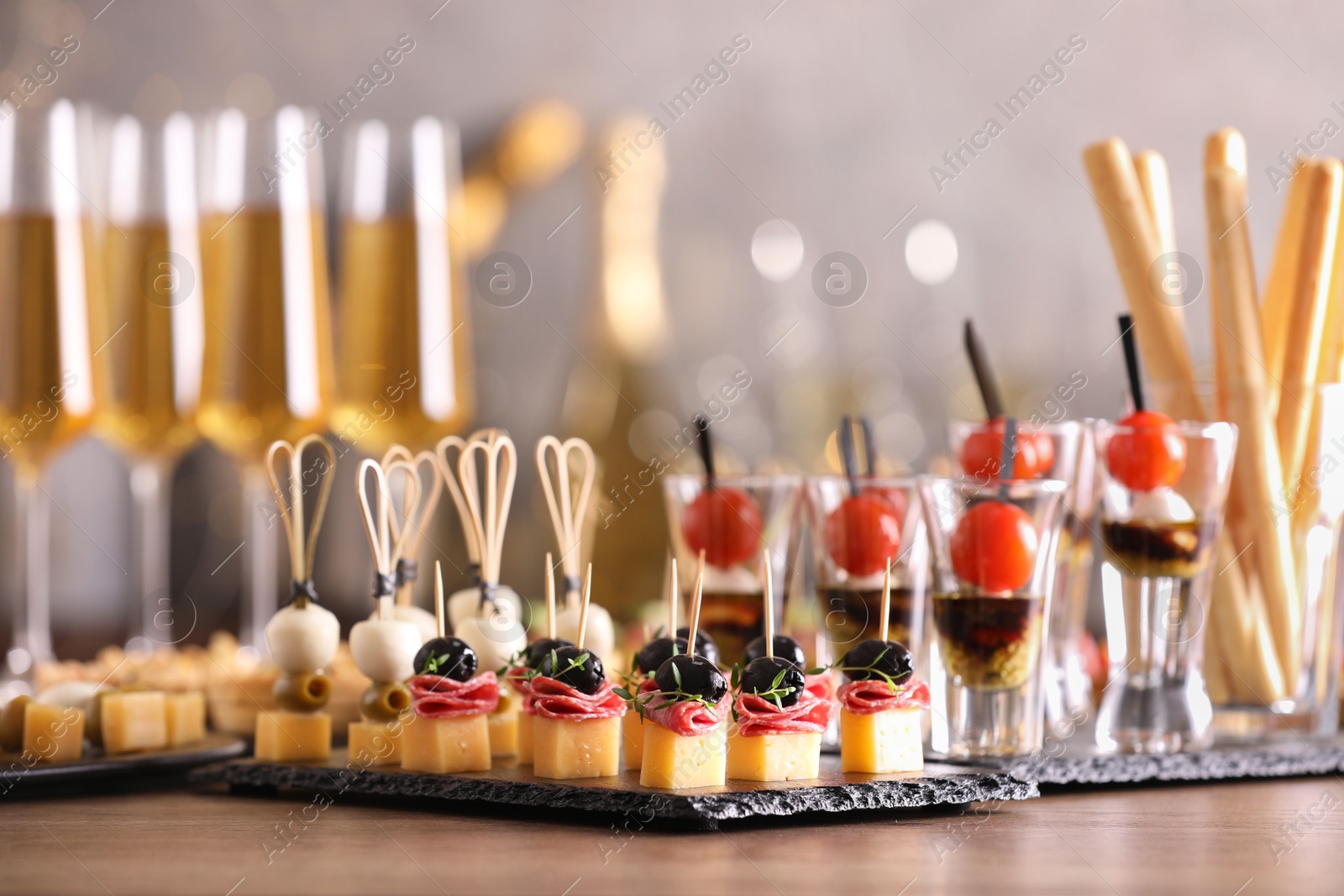 Photo of Many different tasty canapes and wine on wooden table against blurred lights