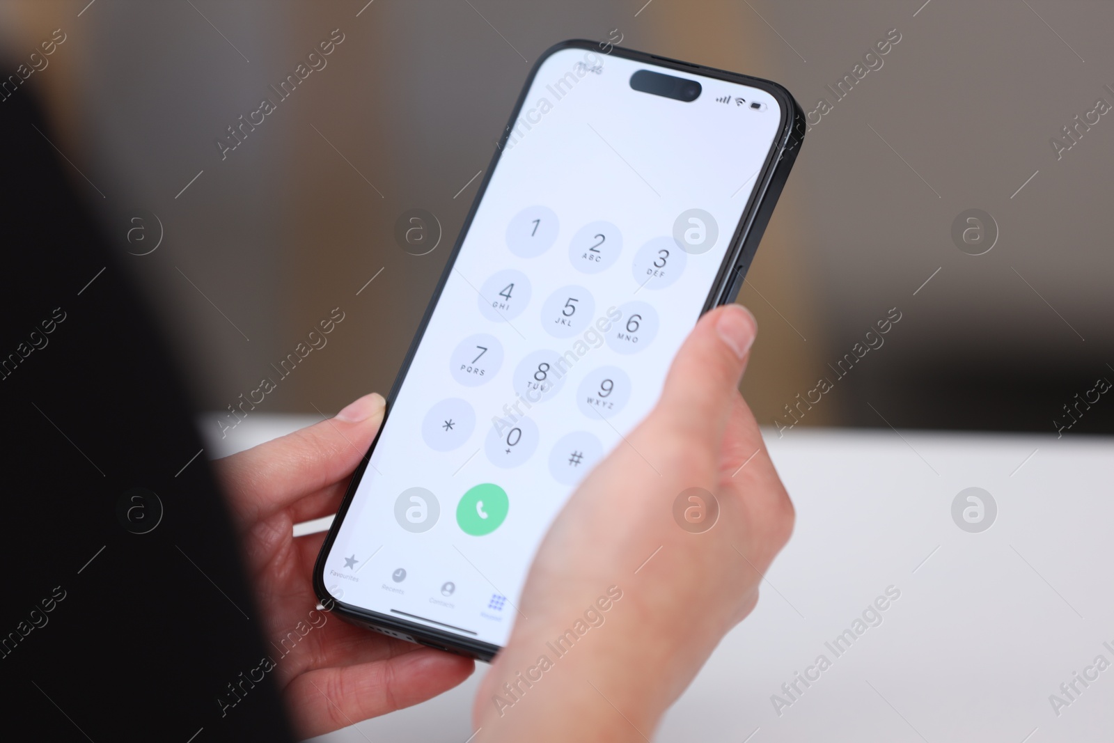 Photo of Woman holding smartphone with dialer application at white table against blurred background, closeup