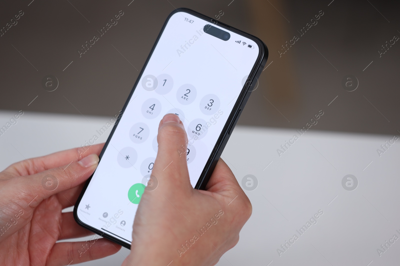 Photo of Woman dialing number on smartphone at white table against blurred background, closeup