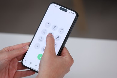 Photo of Woman dialing number on smartphone at white table against blurred background, closeup