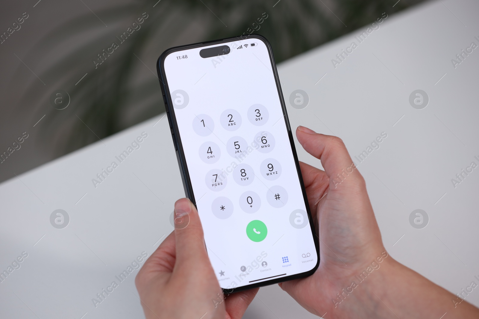 Photo of Woman holding smartphone with dialer application at white table against blurred background, closeup