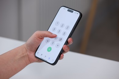 Photo of Woman dialing number on smartphone at white table against blurred background, closeup