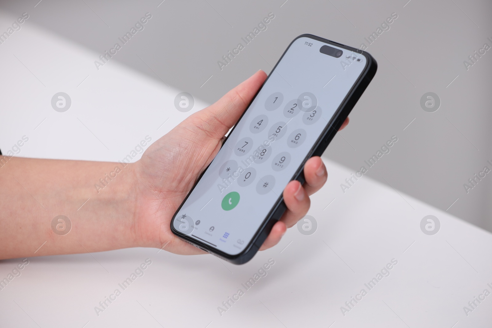 Photo of Woman holding smartphone with dialer application at white table against blurred background, closeup