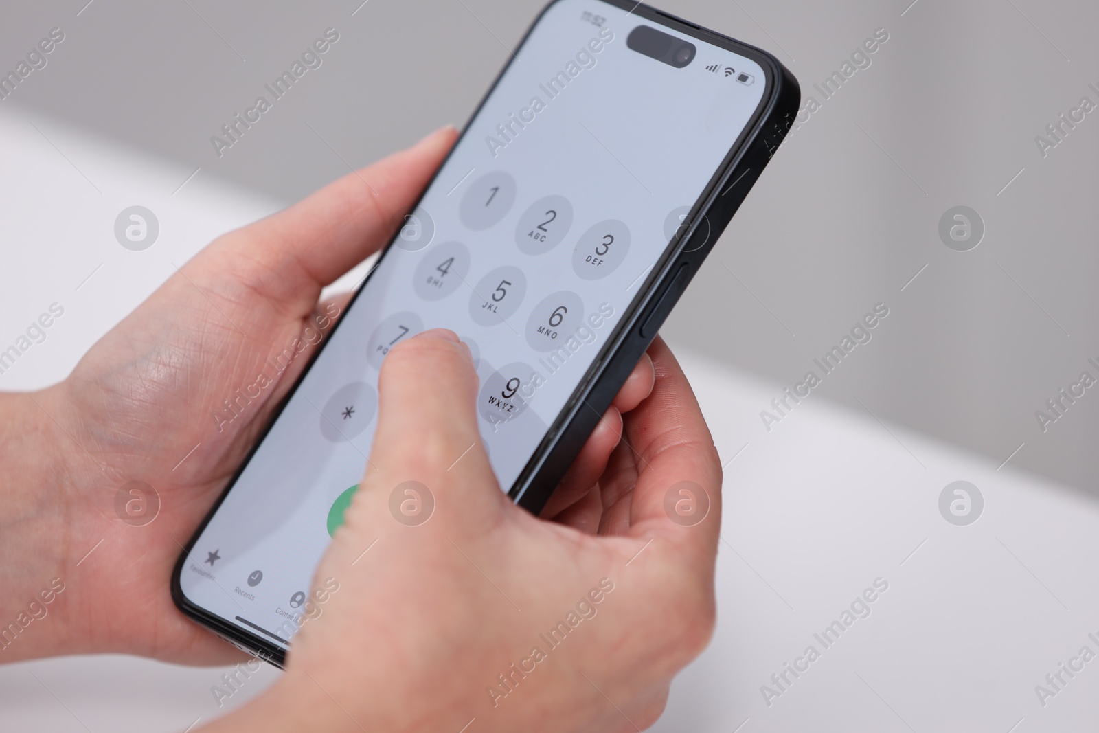 Photo of Woman dialing number on smartphone at white table against blurred background, closeup