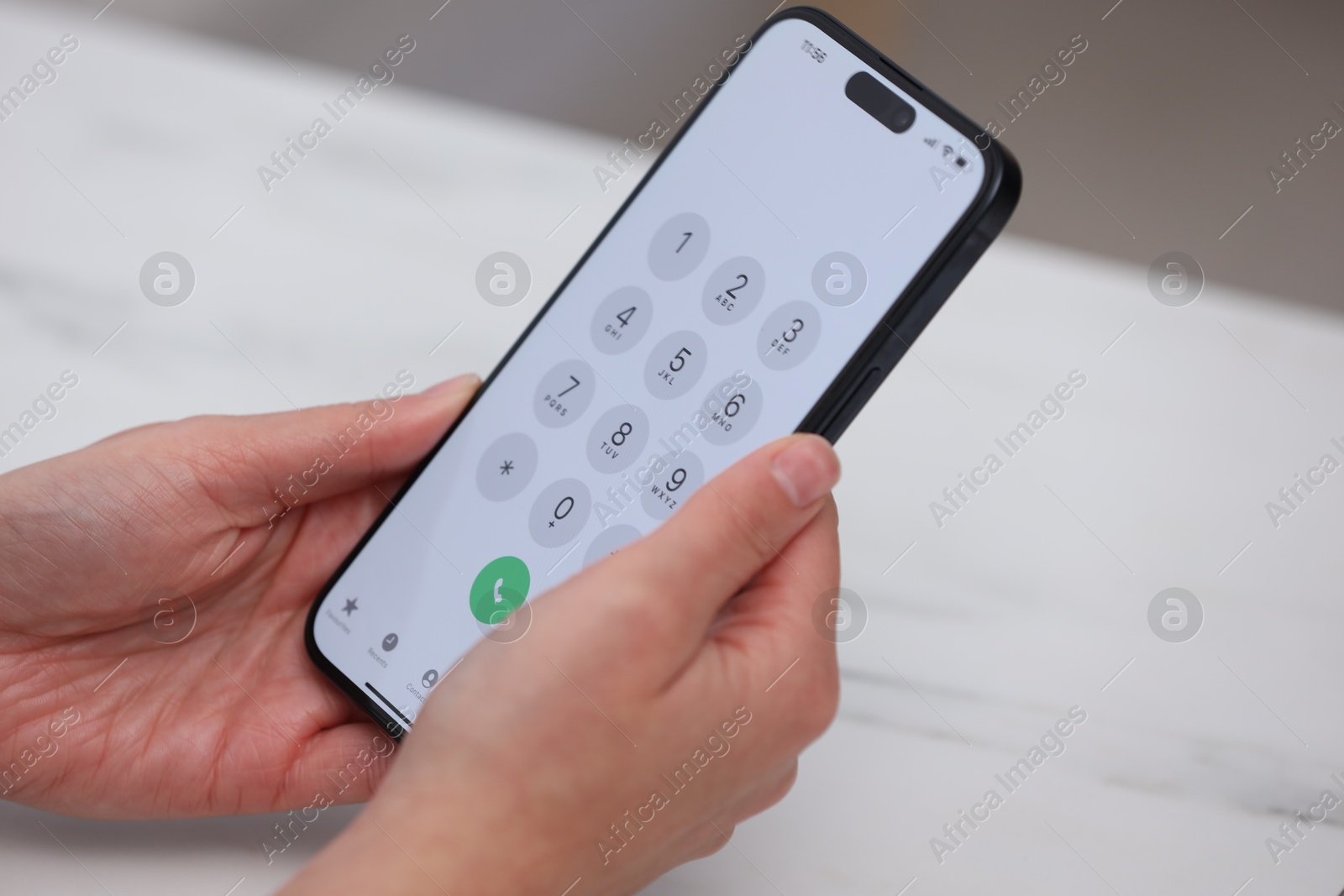 Photo of Woman holding smartphone with dialer application at white table against blurred background, closeup