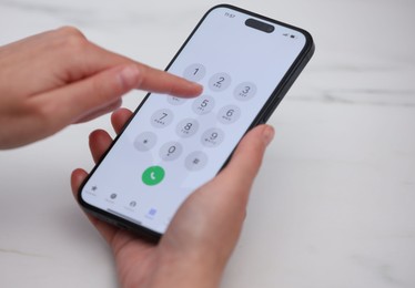 Photo of Woman dialing number on smartphone at white marble table, closeup