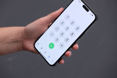 Photo of Woman holding smartphone with dialer application against blurred grey background, closeup