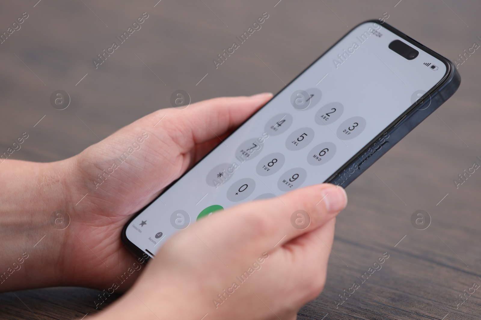 Photo of Woman holding smartphone with dialer application at wooden table, closeup