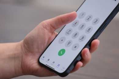 Photo of Woman holding smartphone with dialer application against blurred background, closeup