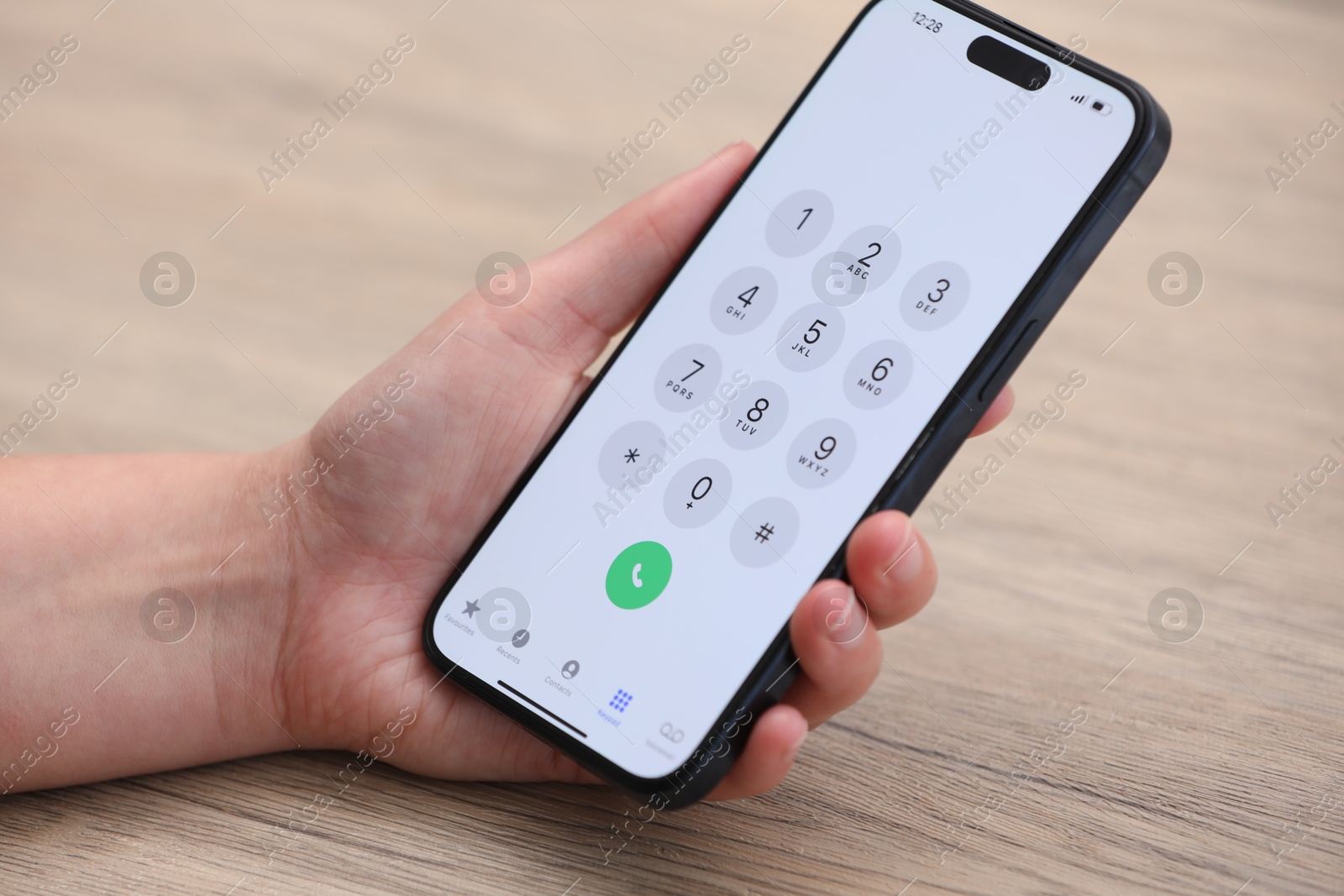 Photo of Woman holding smartphone with dialer application at wooden table, closeup