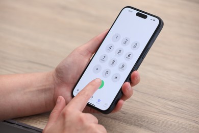 Photo of Woman dialing number on smartphone at wooden table, closeup