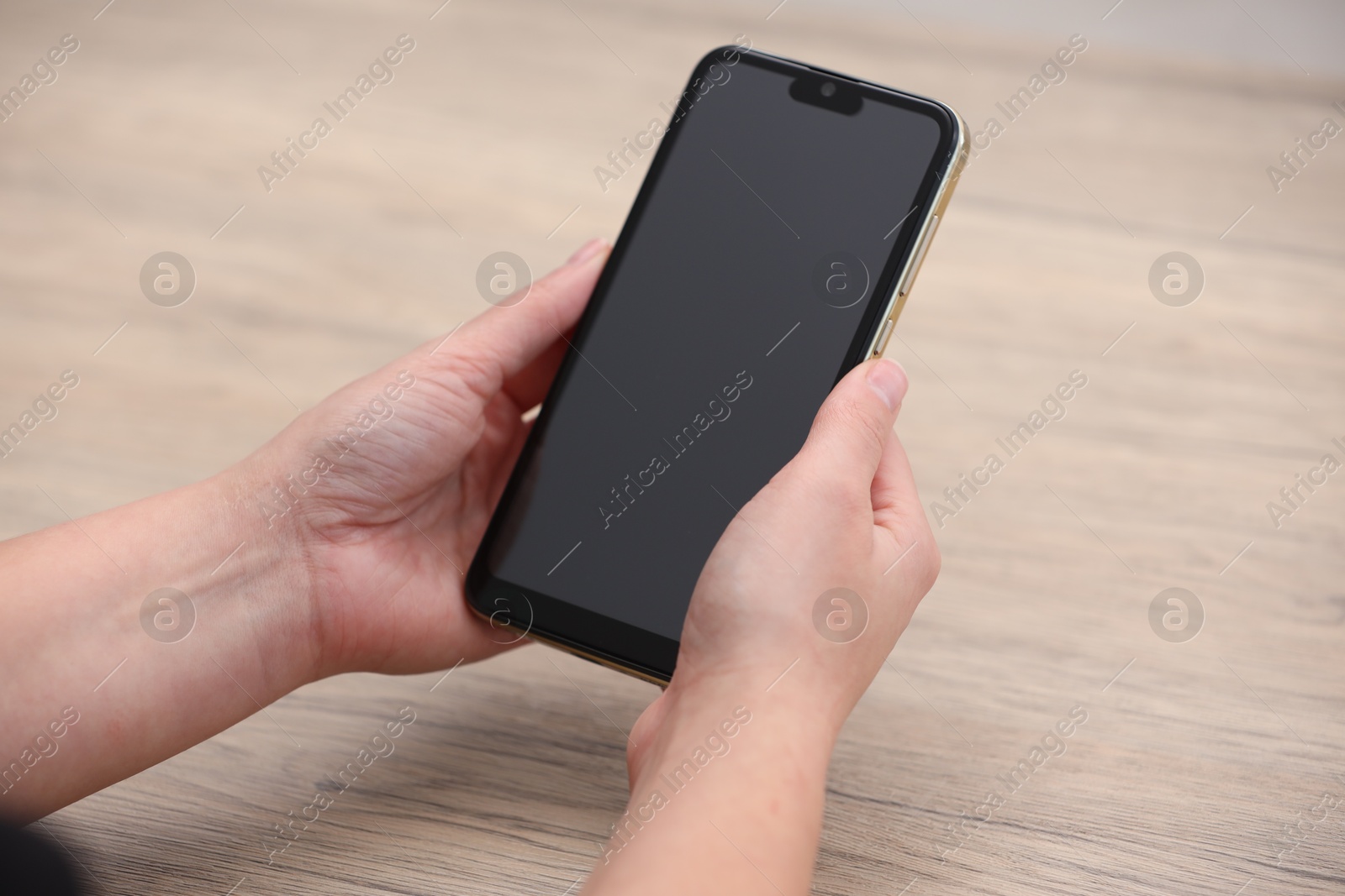 Photo of Woman holding smartphone with blank screen at wooden table, closeup