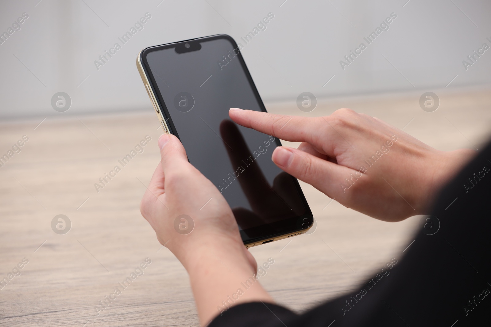 Photo of Woman using smartphone with blank screen at wooden table, closeup