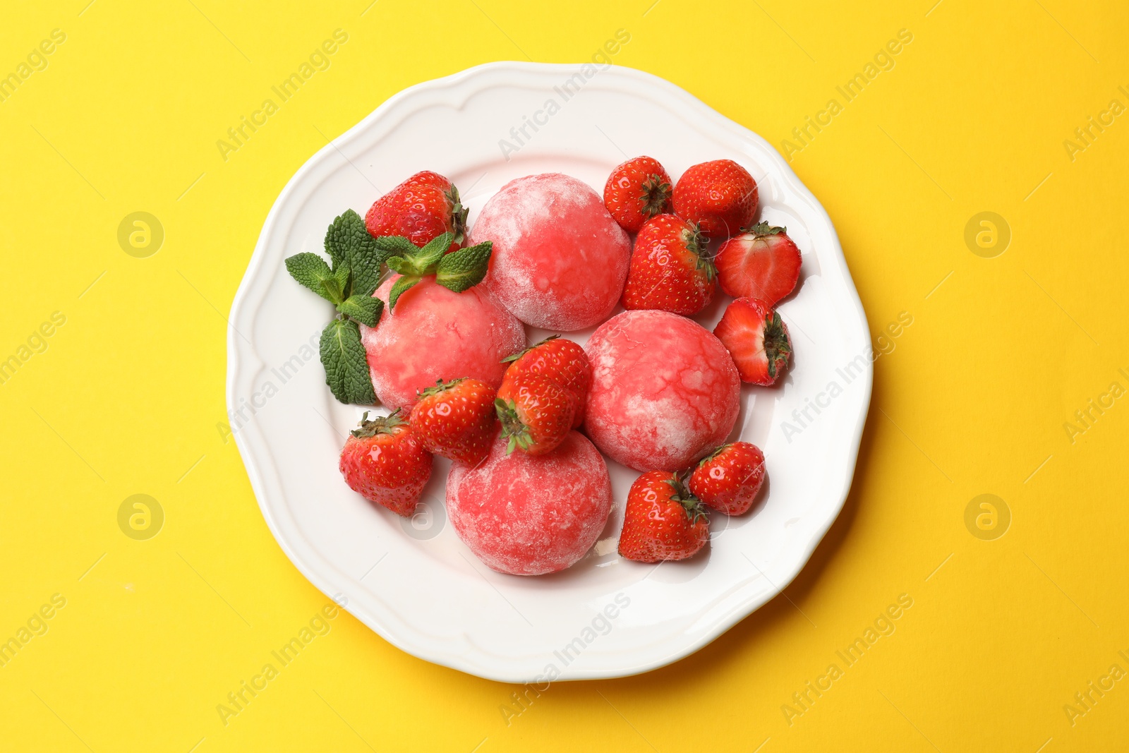 Photo of Delicious mochi, strawberries and mint on yellow background, top view