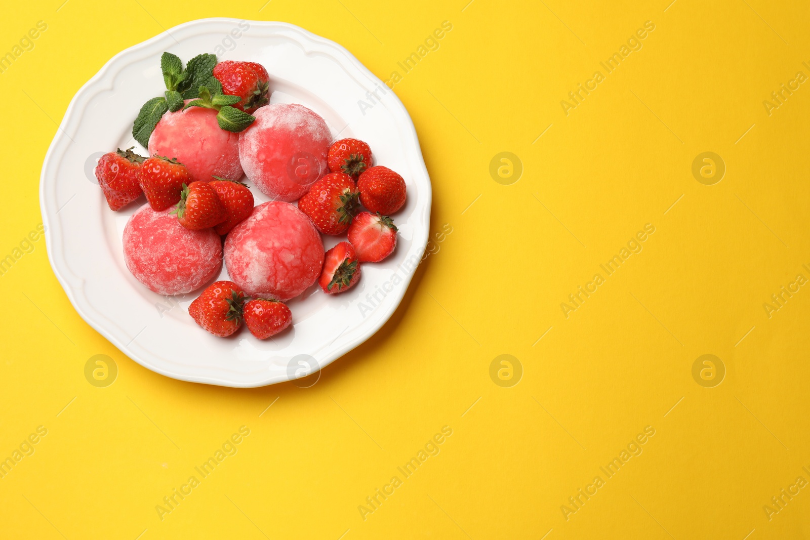 Photo of Delicious mochi, strawberries and mint on yellow background, top view. Space for text