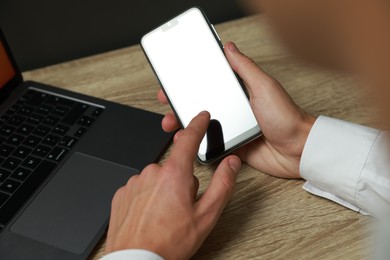 Photo of Man using smartphone with blank screen at wooden table, closeup