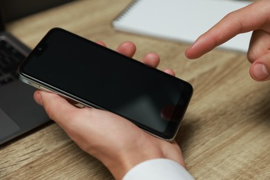 Photo of Man using smartphone with blank screen at wooden table, closeup